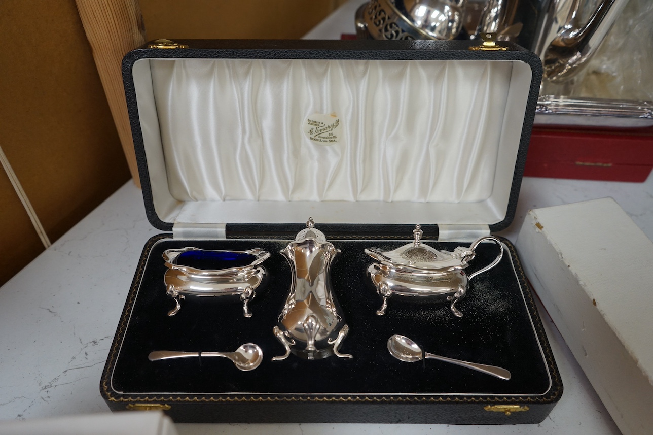 A George V silver cigarette box and assorted plated ware to include a cased cruet, a modern silver wine coaster and an embossed Dutch style tea caddy, largest 23cm wide. Condition - varies